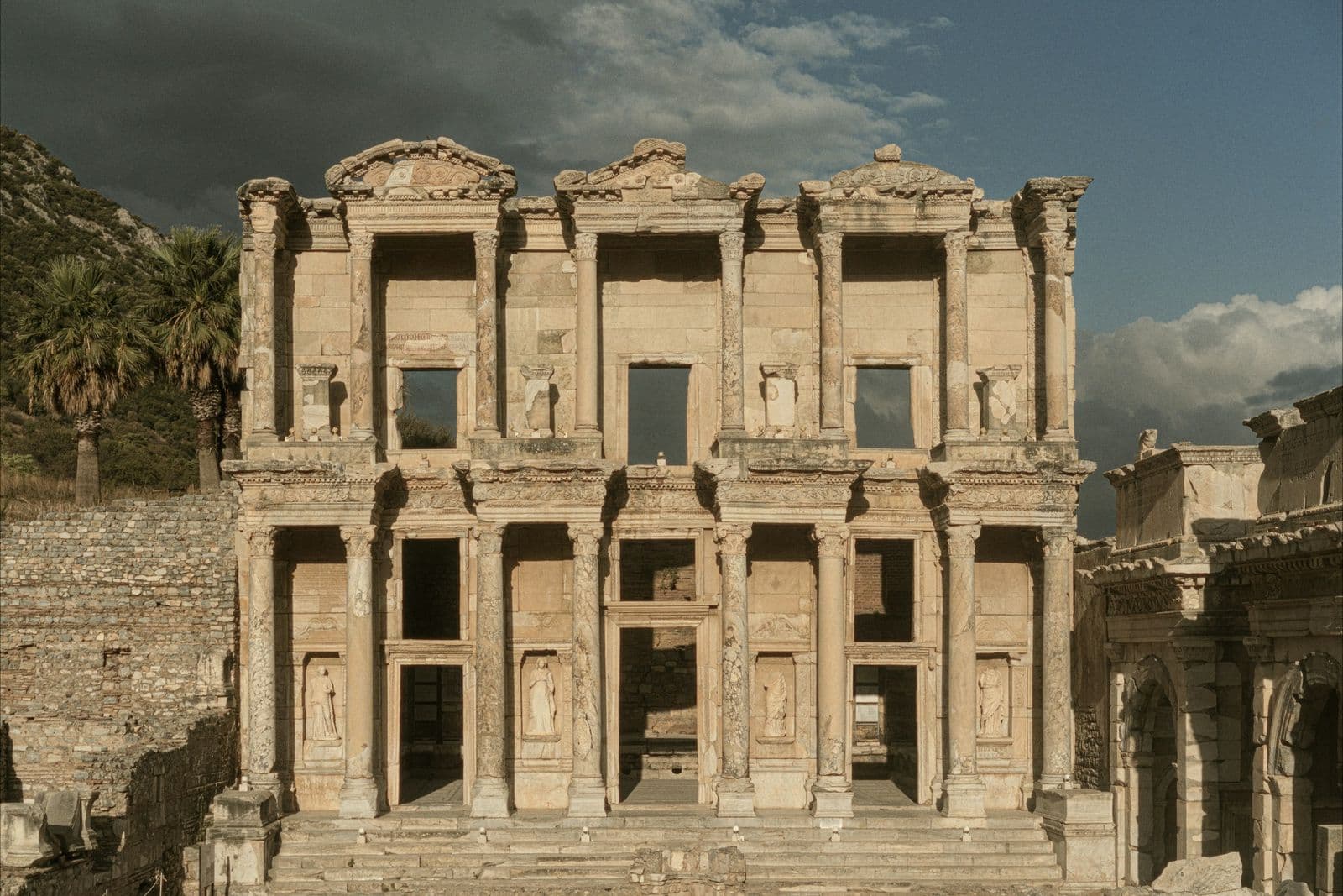 The two-storey facade of the Library of Celsus at Ephesus, lit by low sun under a stormy sky