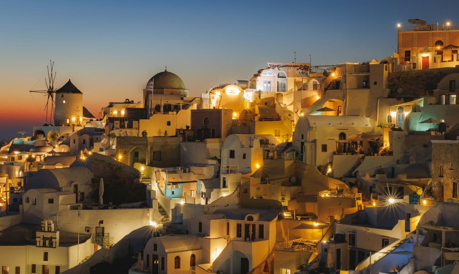 Oia on Santorini at dusk, its houses lit along the rim of the caldera